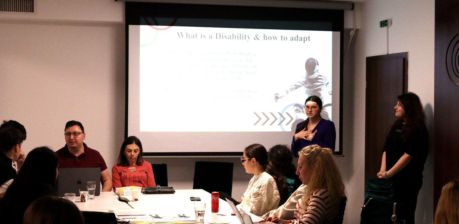 The Romanian team presenting their country's situation next to a slide reading “What is a Disability & how to adapt”.