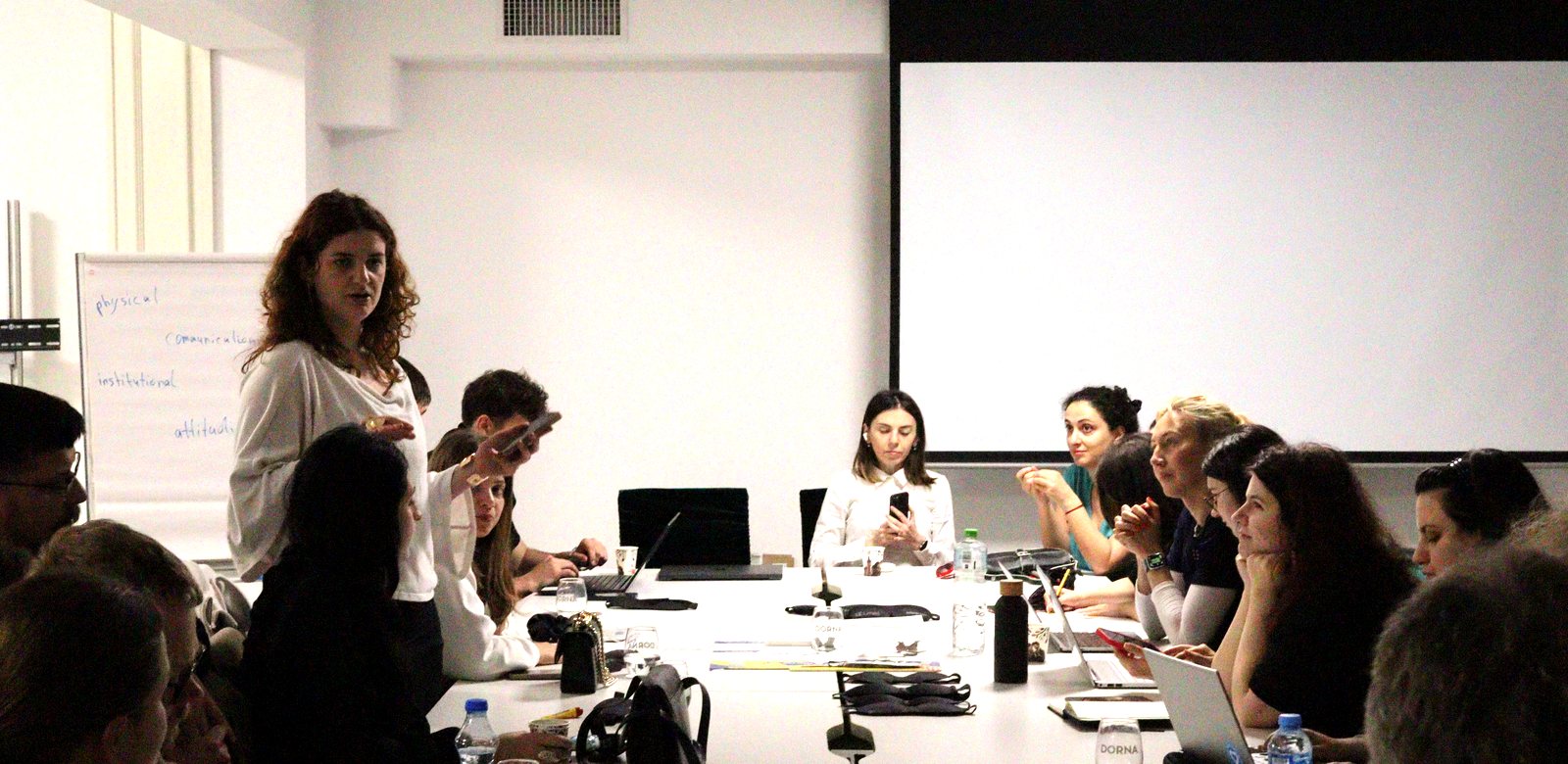 A member of the Serbian team standing to present their country's situation to the group around the table.