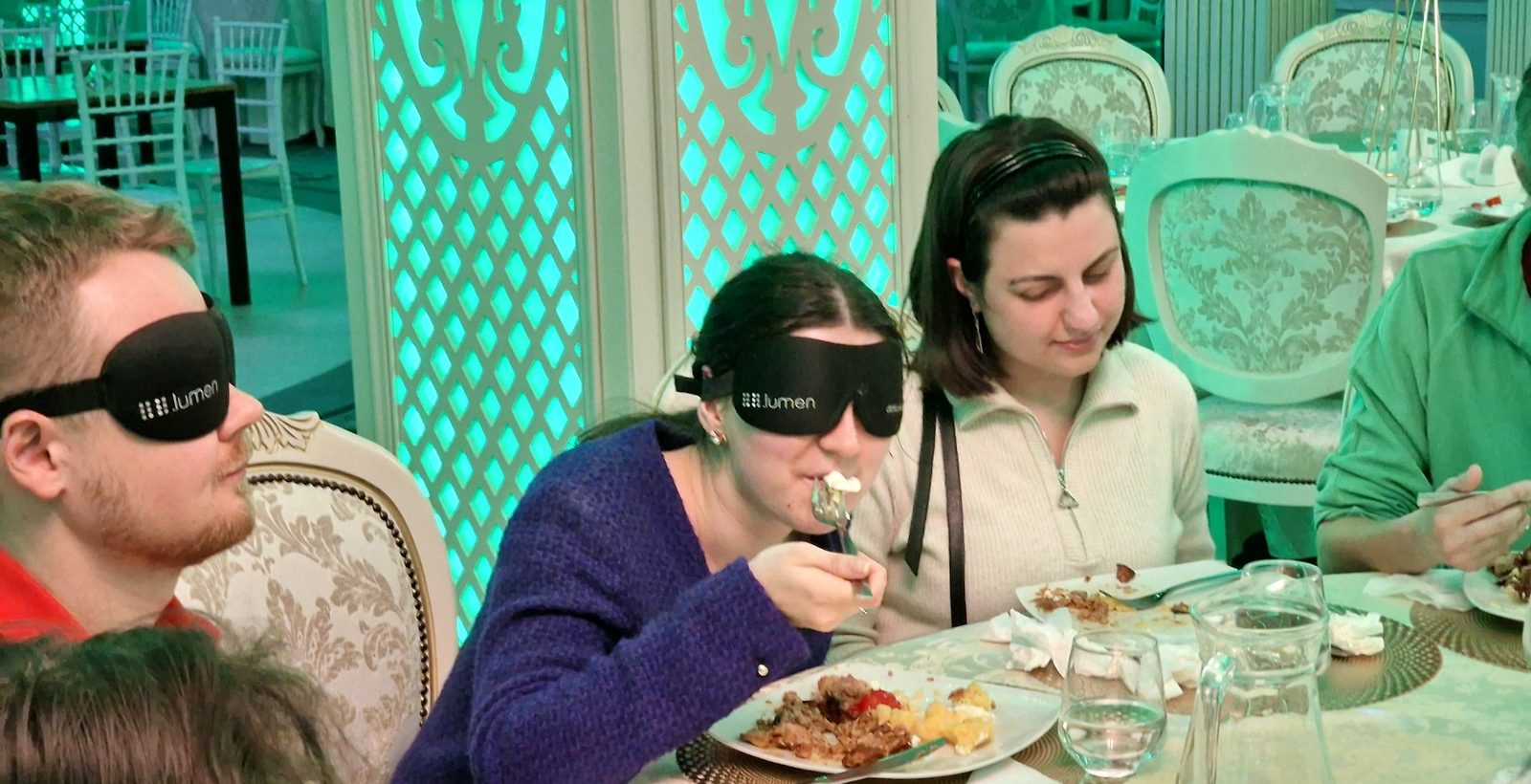 A participant wearing an eyeshade tastes her meal at the festively set table.