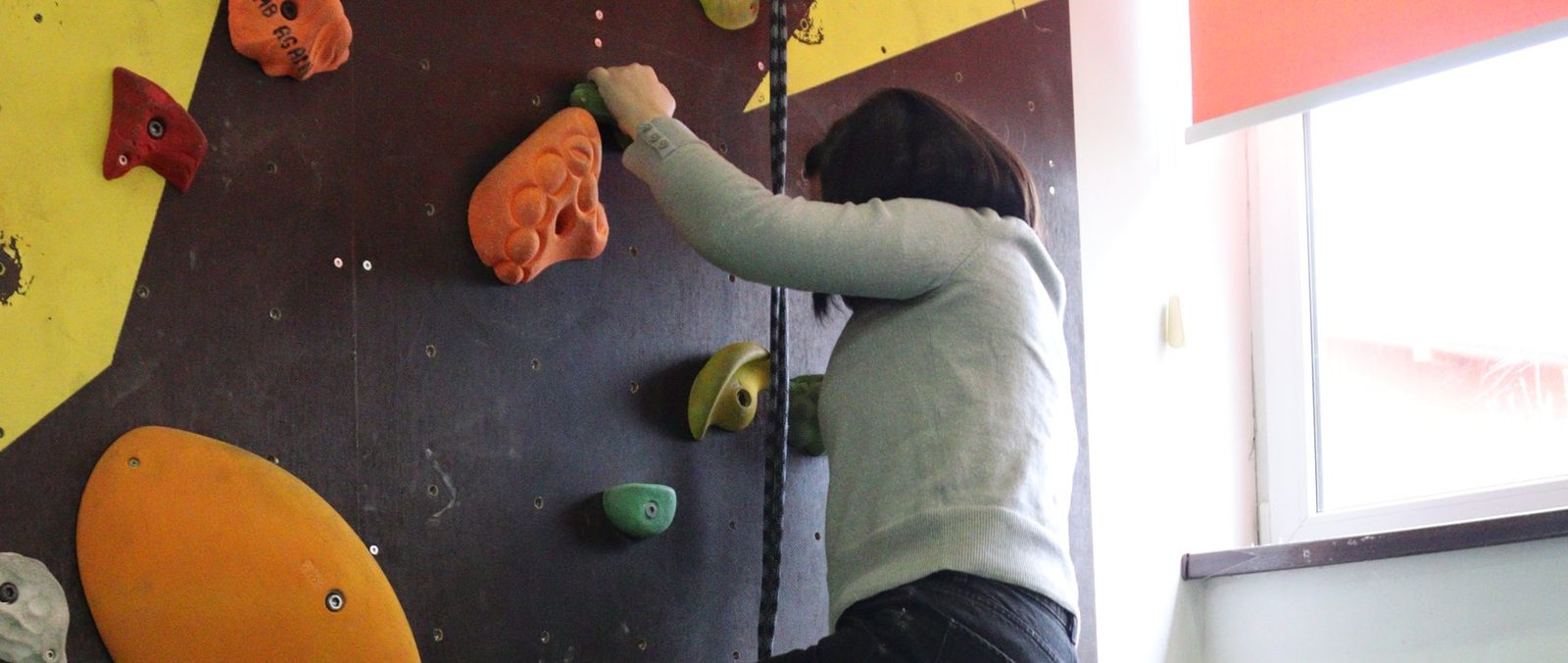 A participant climbs an indoor climbing wall; a white cane leans against the wall below.