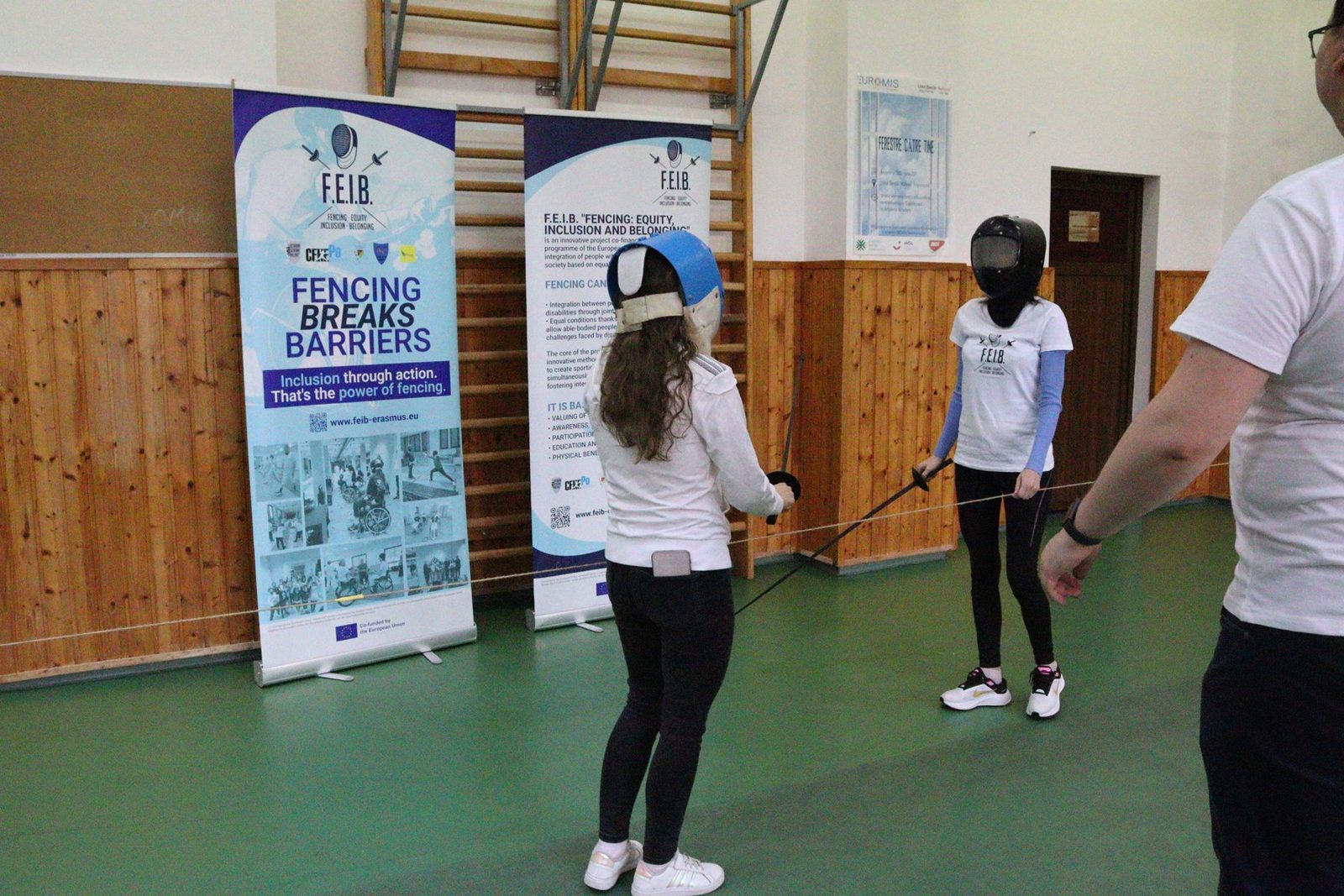 Two participants in fencing masks practise with foils.