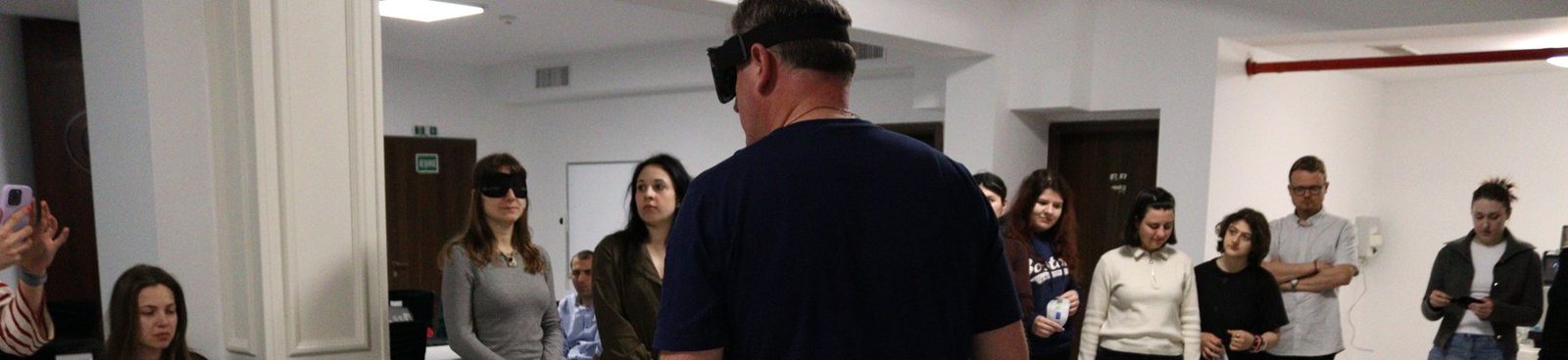A blindfolded participant dribbles a sound football across the room.